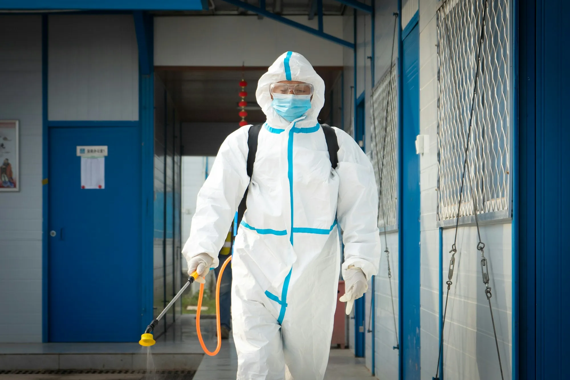Technician in a protective suit spraying disinfectant in a corridor